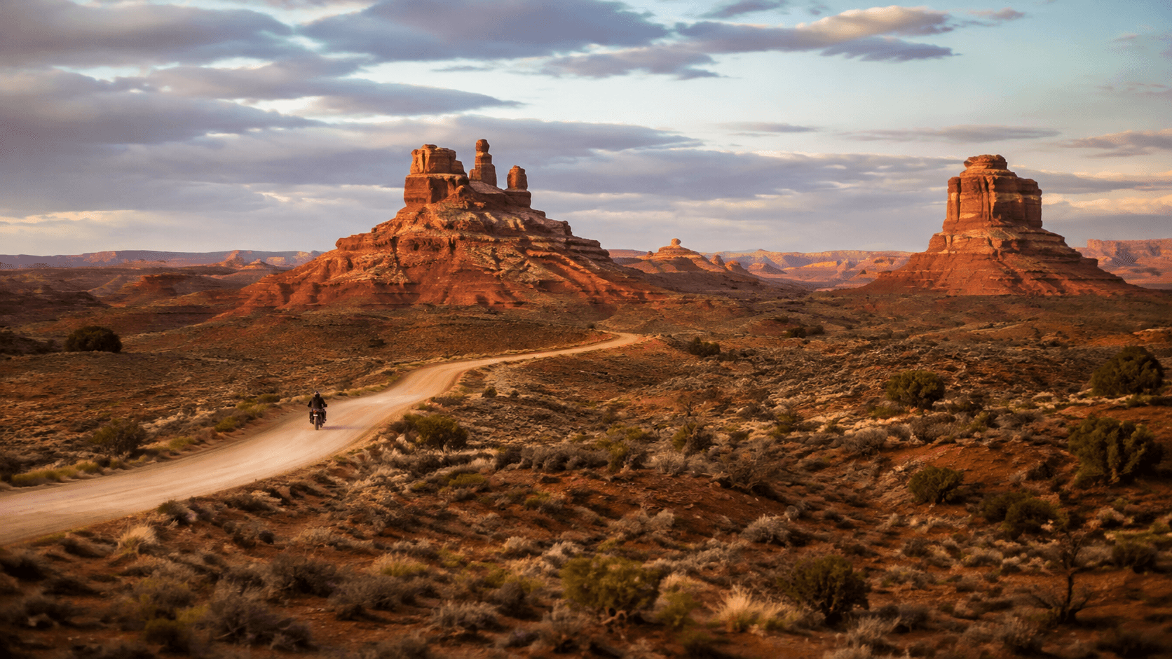 An adventure motorcycle crossing a graded desert road between Utah sandstone buttes